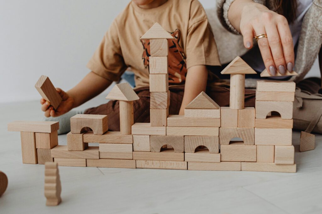 child and adult playing with wooden building blocks.