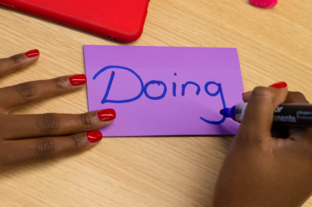 Person writing the word doing on a piece of paper