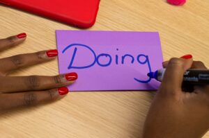 Person writing the word doing on a piece of paper
