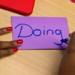 Person writing the word doing on a piece of paper