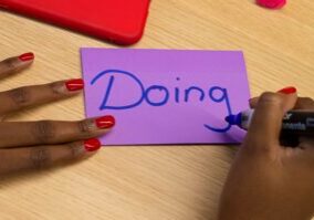 Person writing the word doing on a piece of paper
